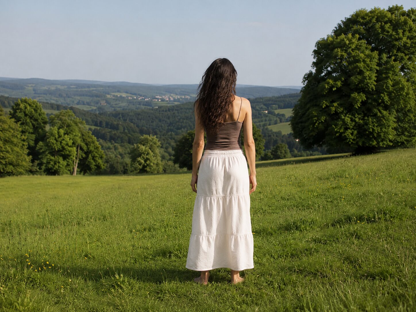 Eine Frau steht barfuß auf einer Wiese und blickt über eine hügelige Landschaft